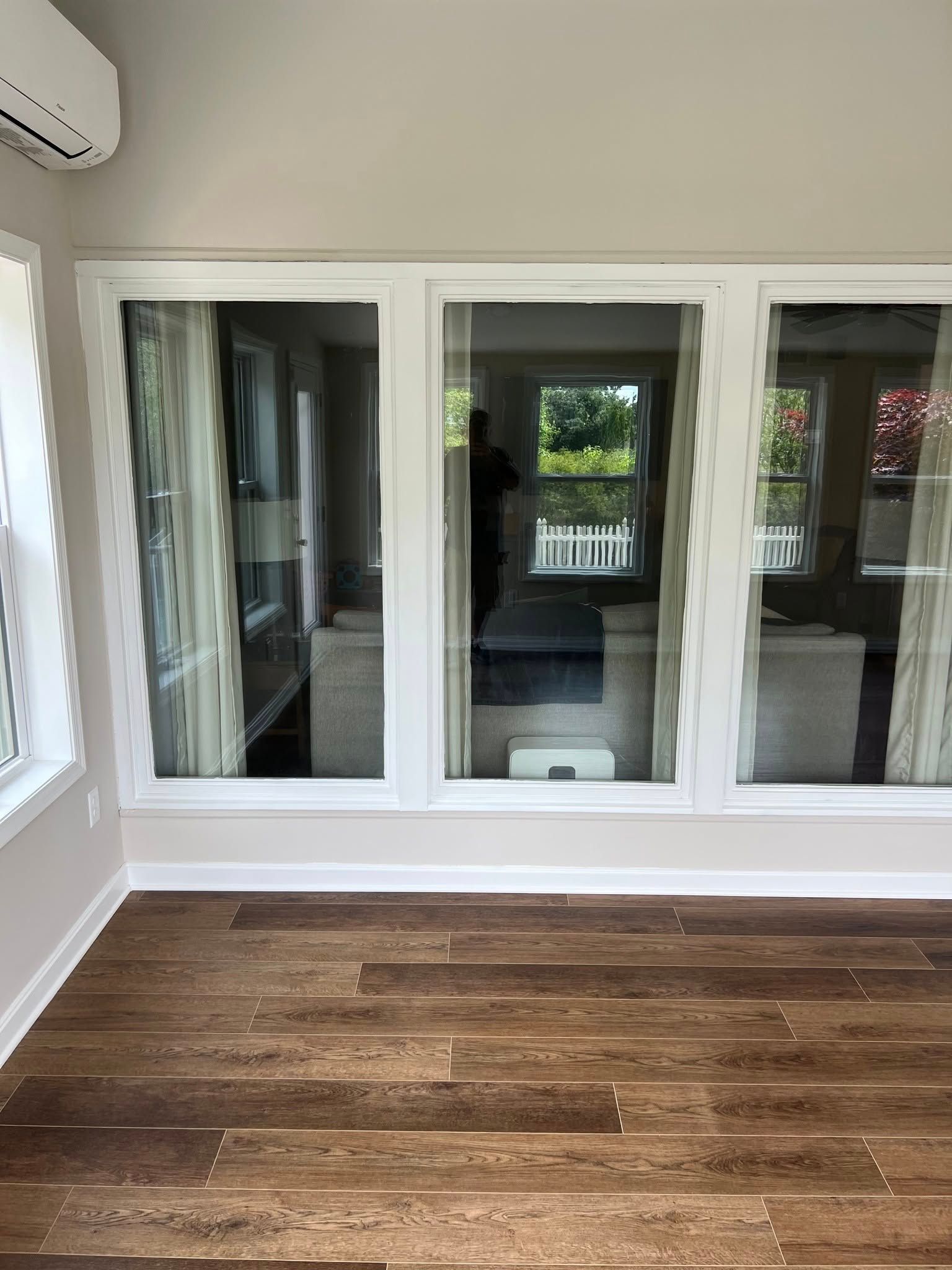 Sunroom with hardwood floor, three large windows, and white trim. Exterior view reflects outdoors.