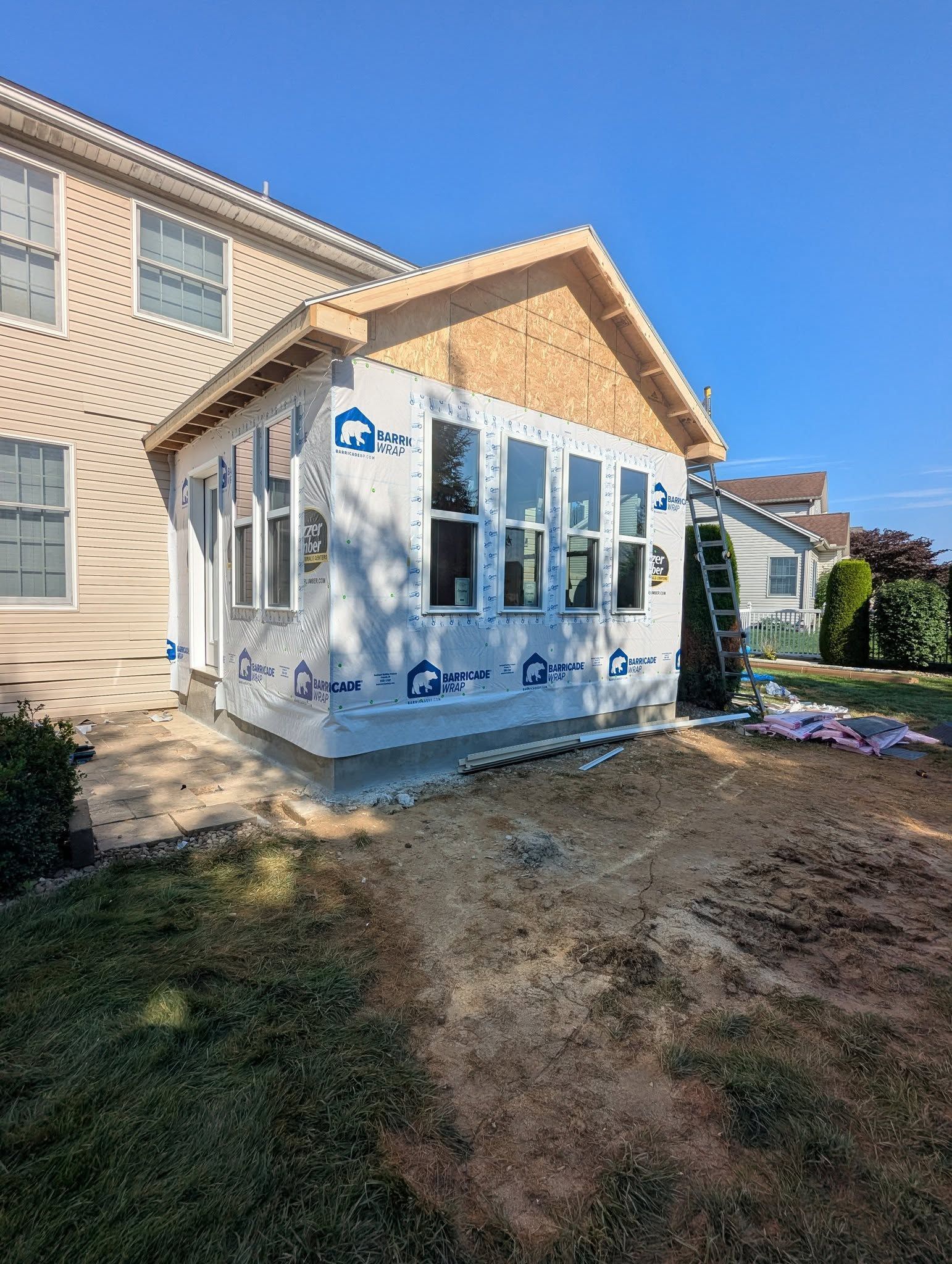 Sunroom addition under construction, attached to a tan house; blue wrap, windows installed.