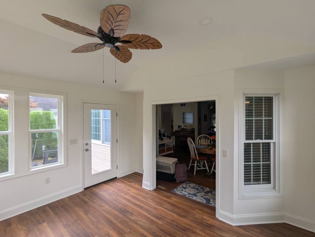 Sunroom with windows and door. Brown ceiling fan, hardwood floor, open doorway to dining area.