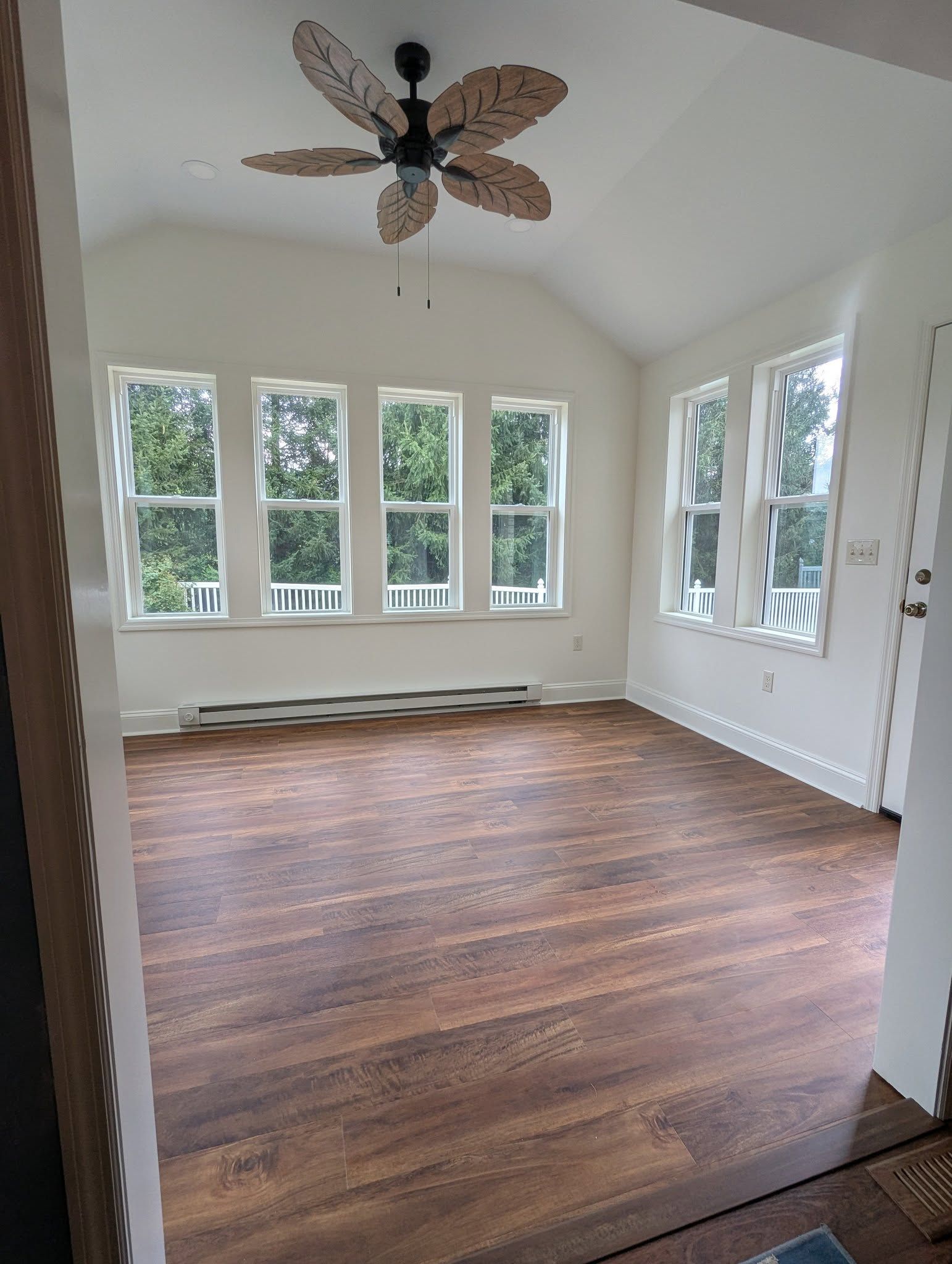 Sunroom with wood floor, white walls, large windows, and a ceiling fan.