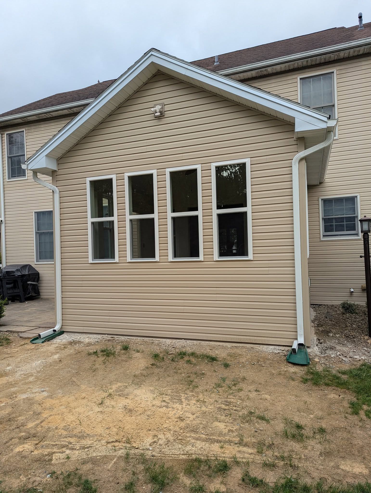 Tan-sided house addition with three windows. Brown roof, white trim and gutters. Dry grassy area in front.