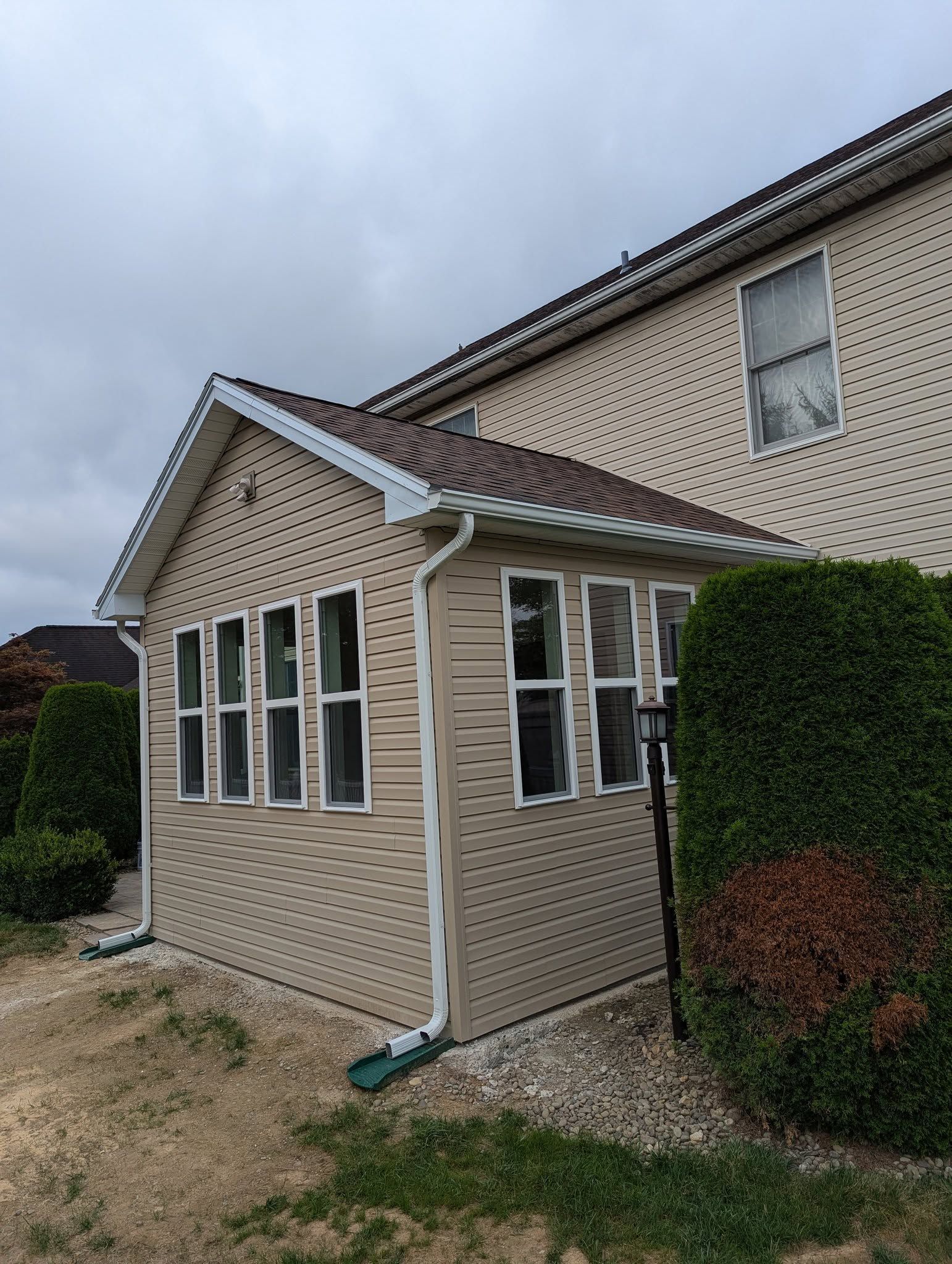Tan sunroom addition with windows, attached to a beige house, under a cloudy sky.
