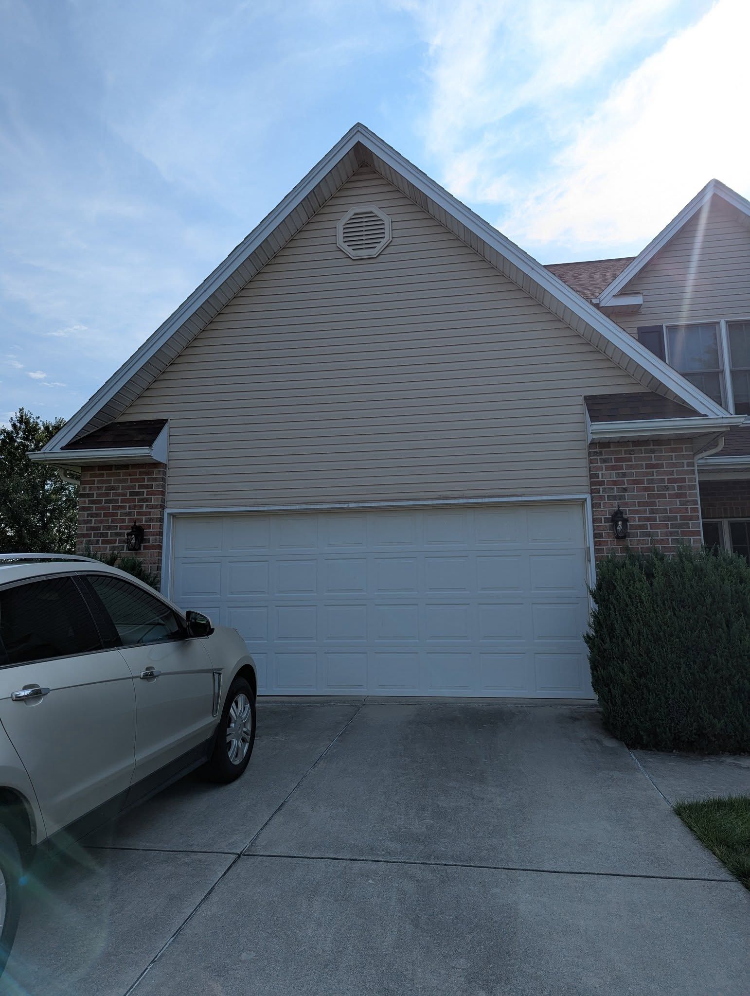 Tan house with a white garage door, a round window, and a car parked in the driveway.