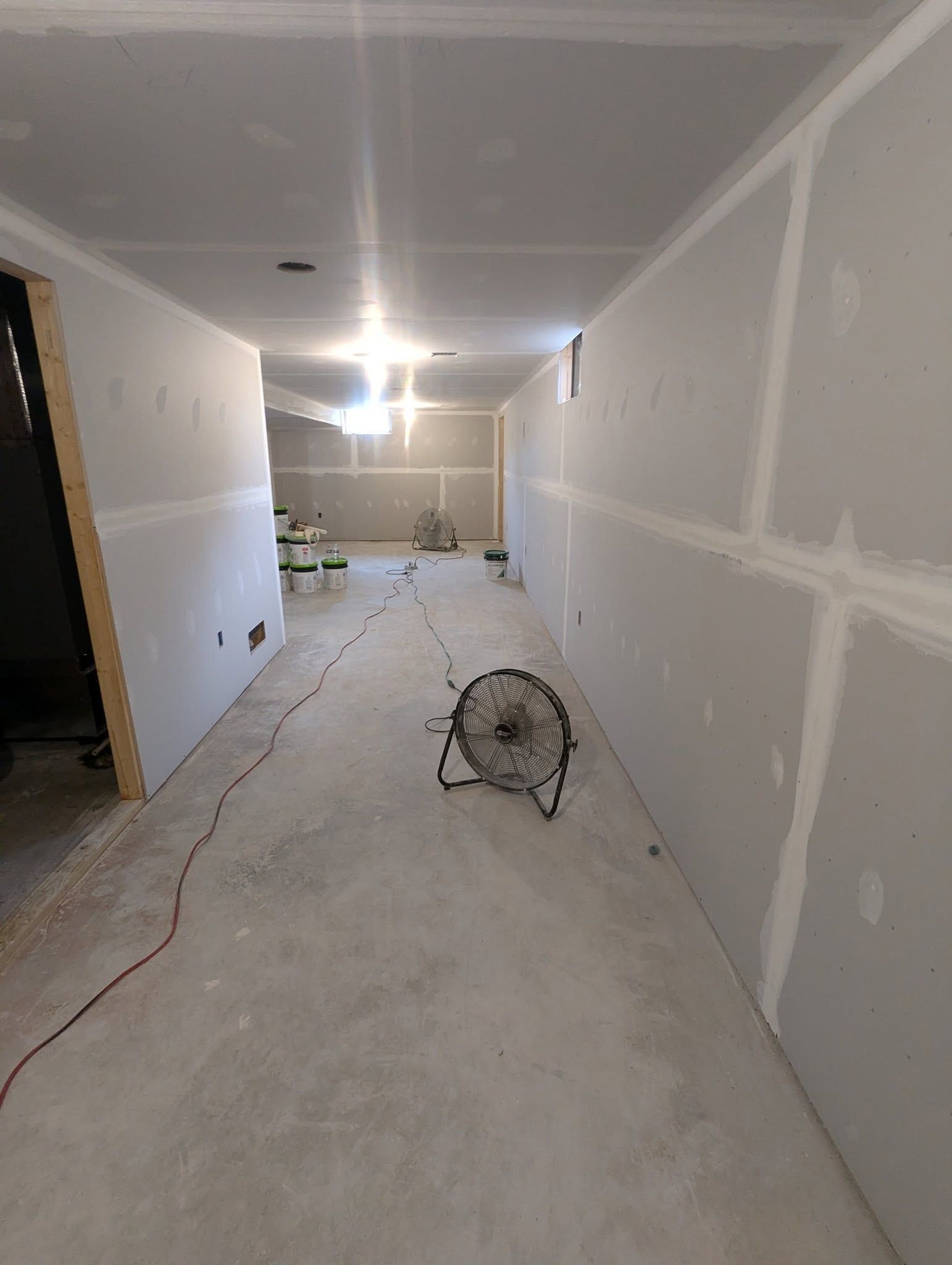 Hallway under construction with drywall and a fan.