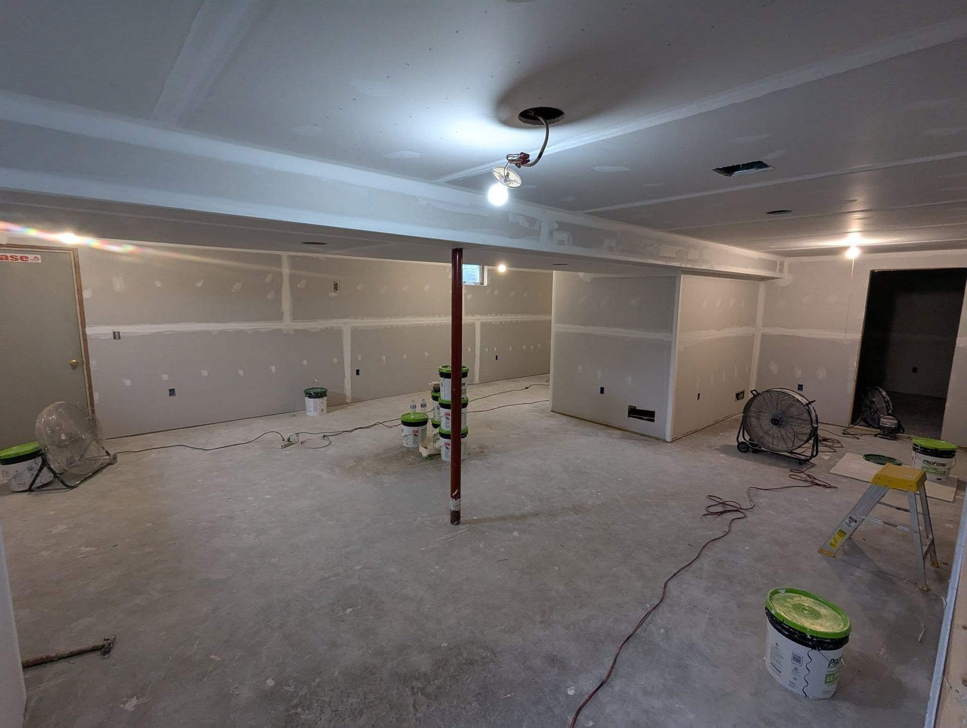 Basement under renovation with drywall installed, unfinished concrete floor, and tools scattered about.