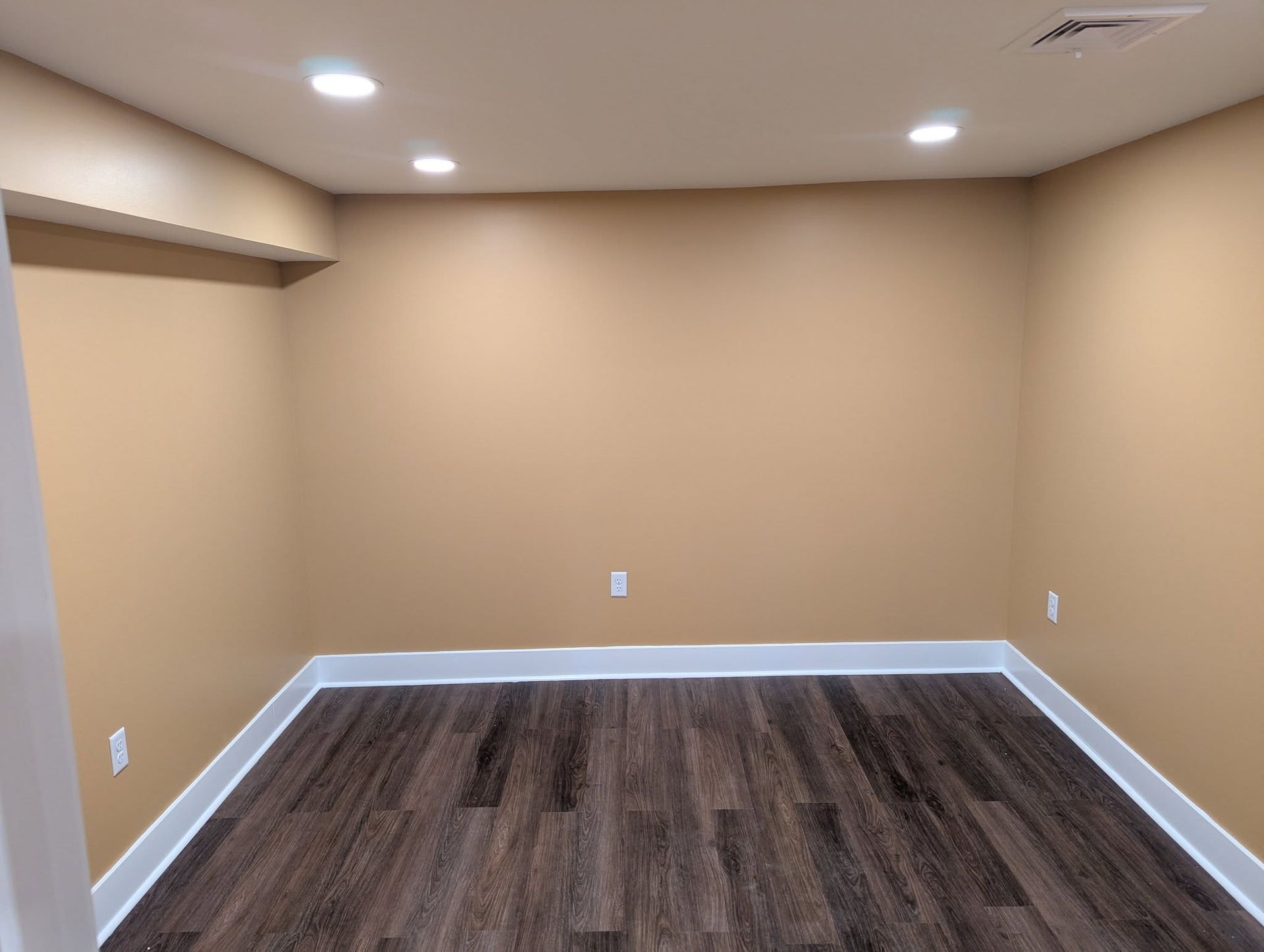 Empty room with brown walls, dark wood floor, and white trim.