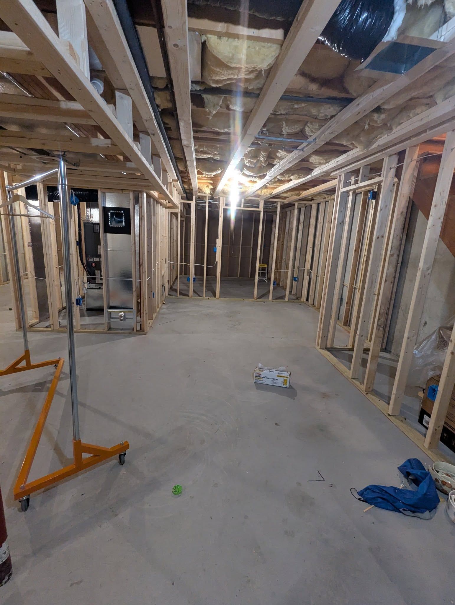 Basement renovation in progress, framing walls. HVAC unit visible. Concrete floor, exposed ceiling.