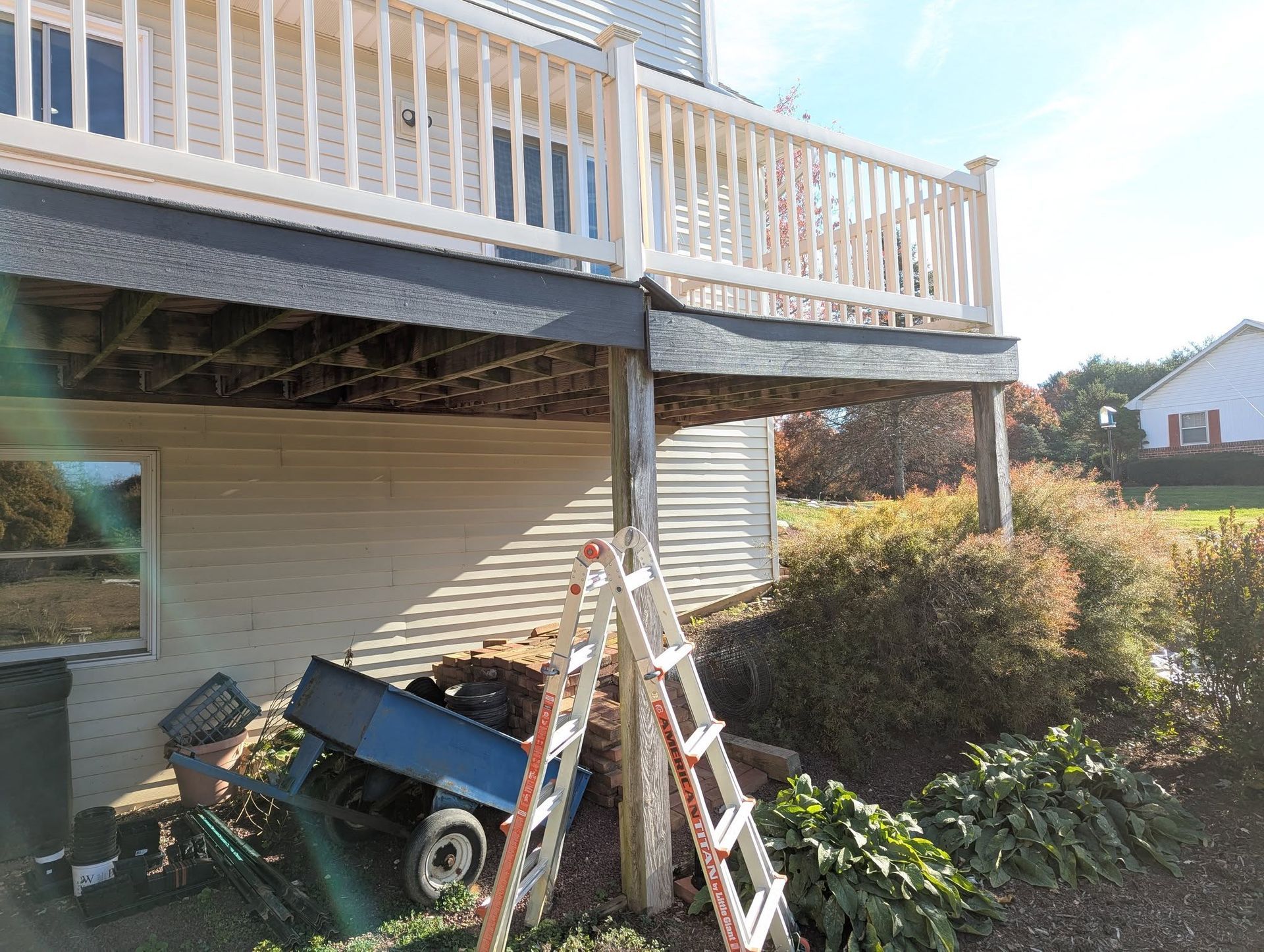Deck of a house with a ladder and cart underneath.