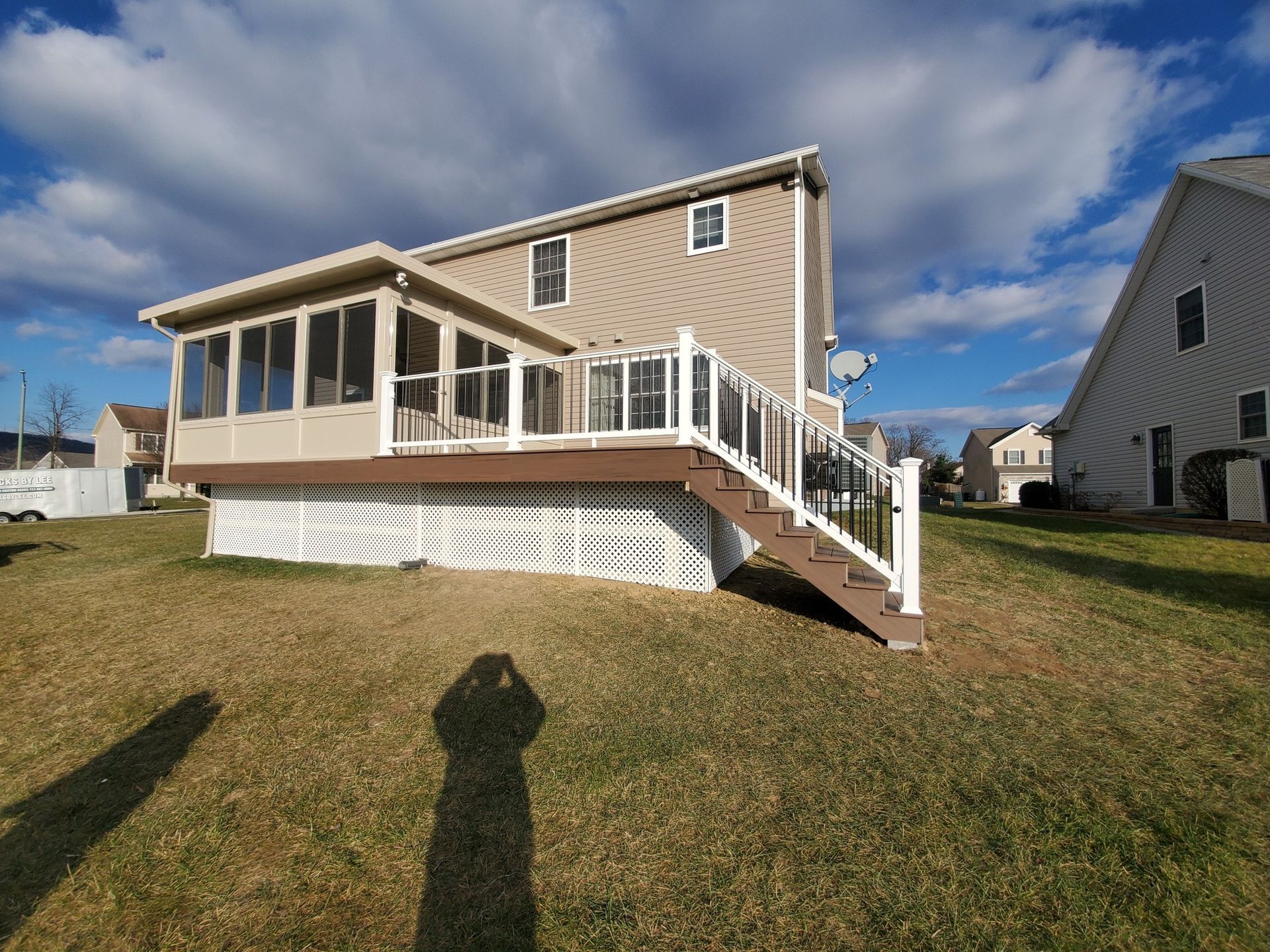 Backyard view of a house with a screened porch and deck. White lattice skirting and brown deck boards. Sunny day.