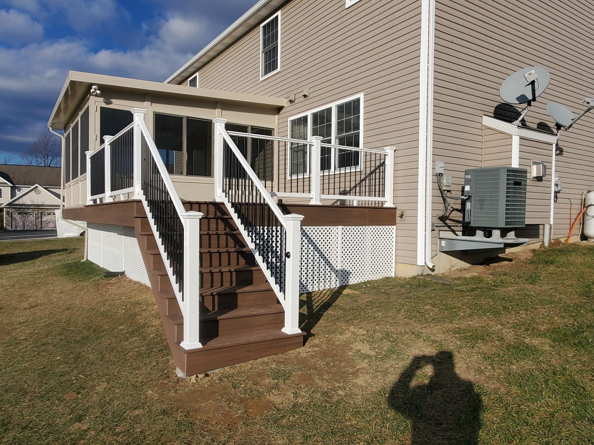 Backyard deck with stairs leading to a screened porch attached to a tan two-story house.