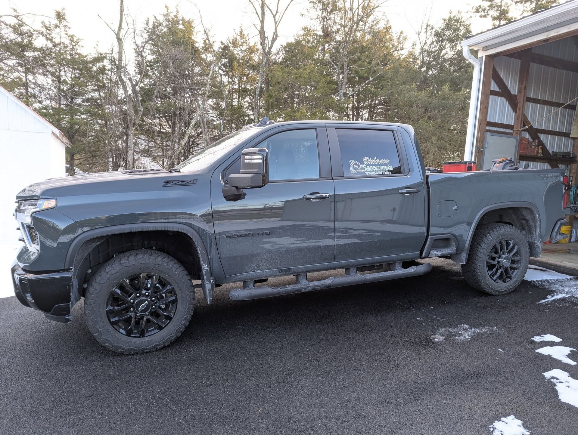 Dark gray Chevrolet truck parked on a driveway near a building with snow on the ground.