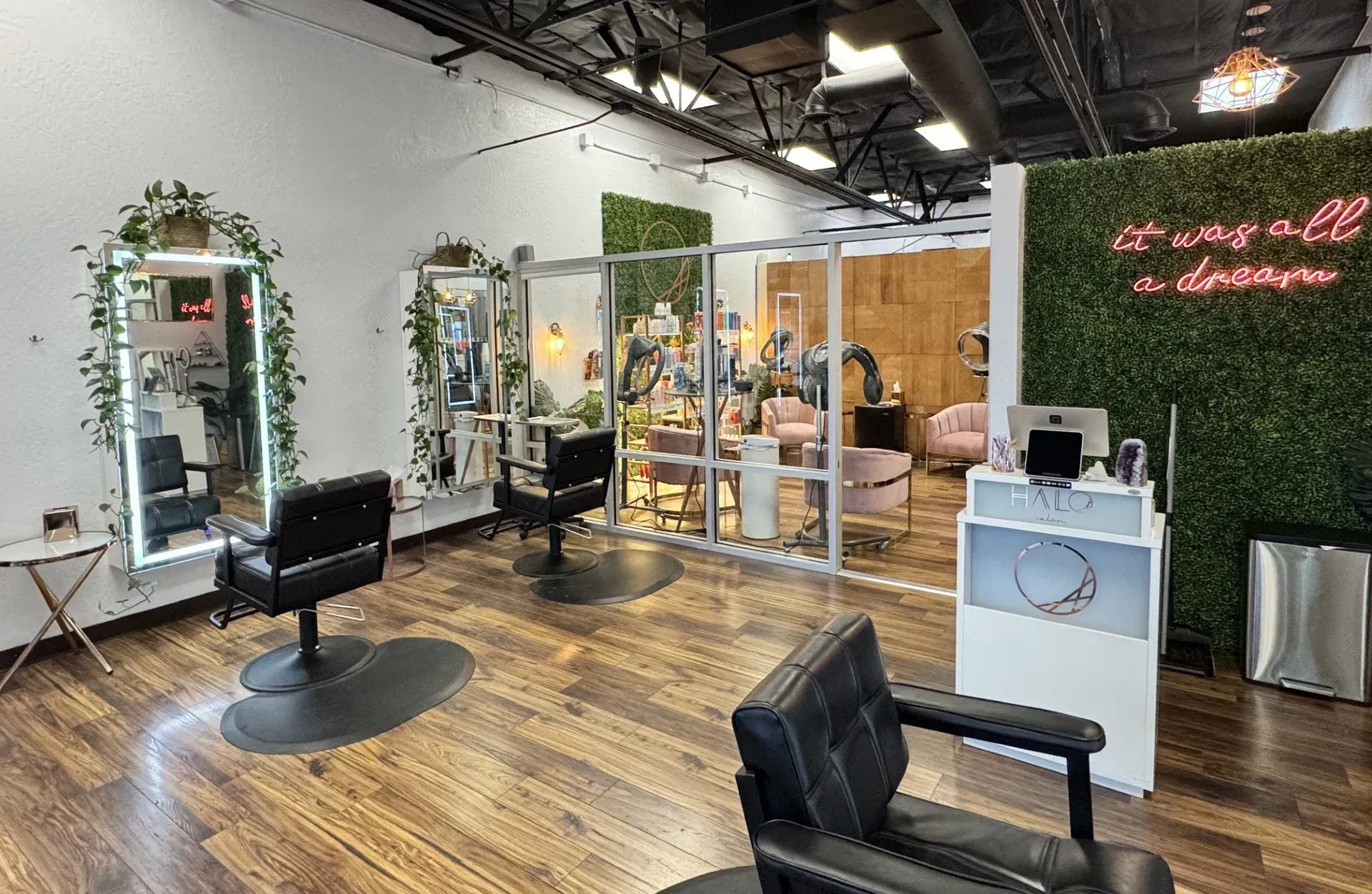 Hair salon interior with styling stations, mirrors, and decorative greenery.