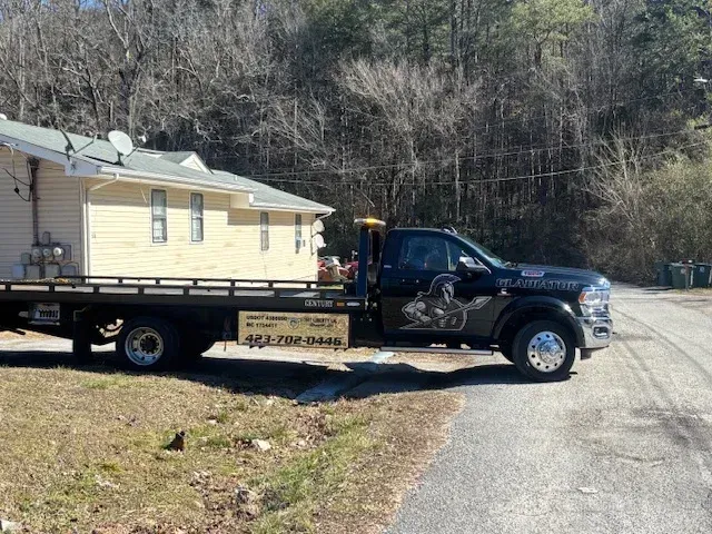 Tow truck hauling a yellow house on a flatbed in a wooded roadside area