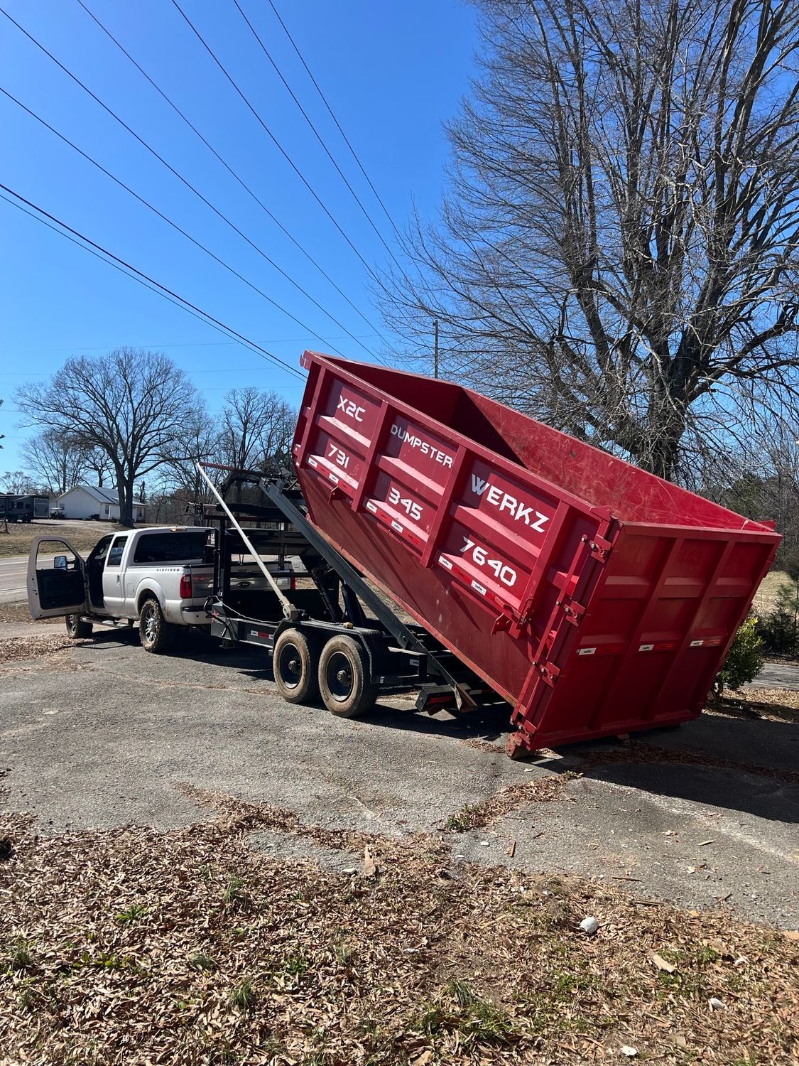A red dumpster is being towed by a truck.