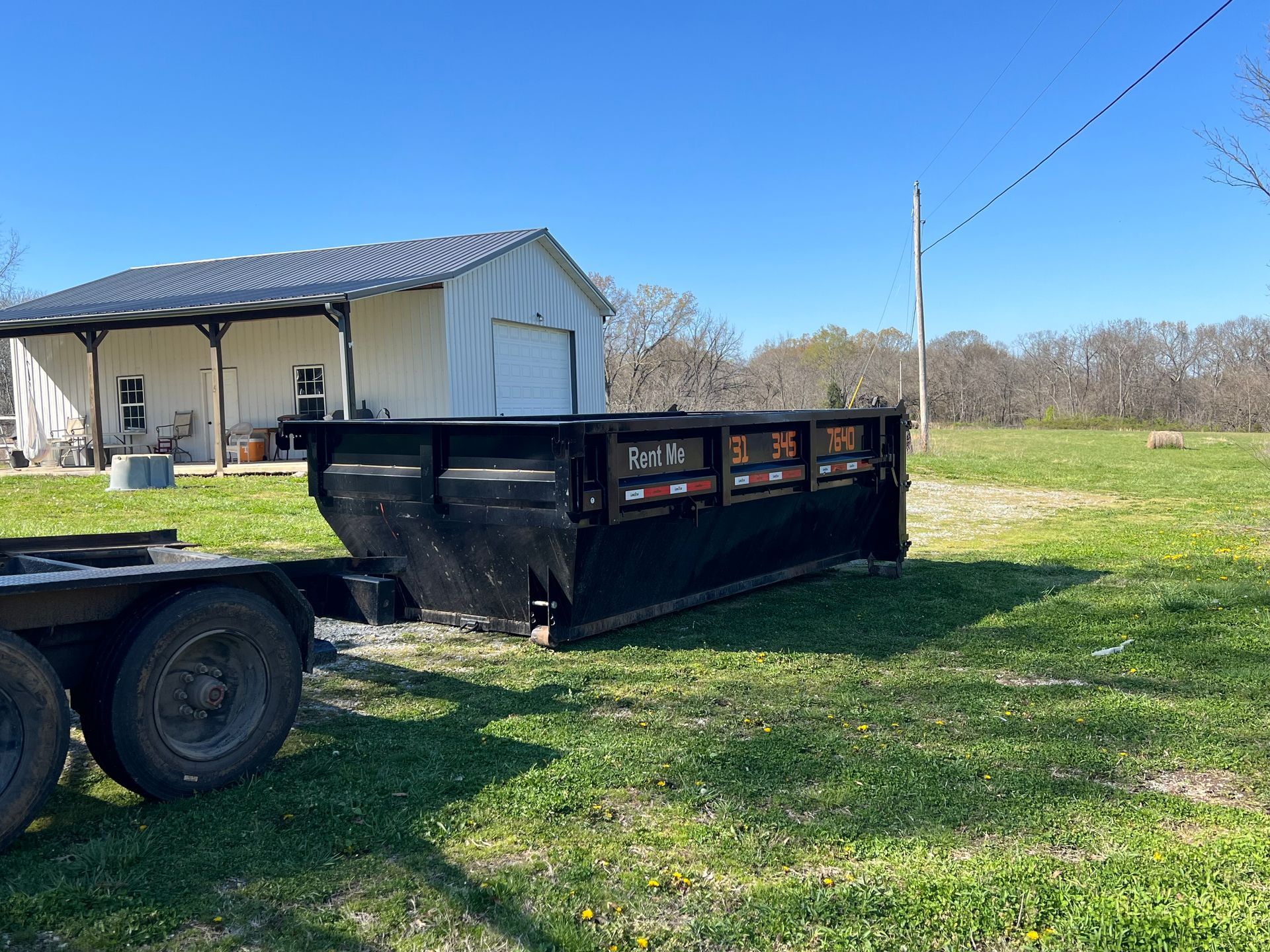 A white truck is towing a red dumpster in a grassy field.