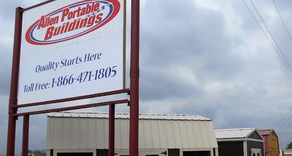 Sign for Allin Portable Buildings with buildings in the background. The sign is white with red and blue lettering.