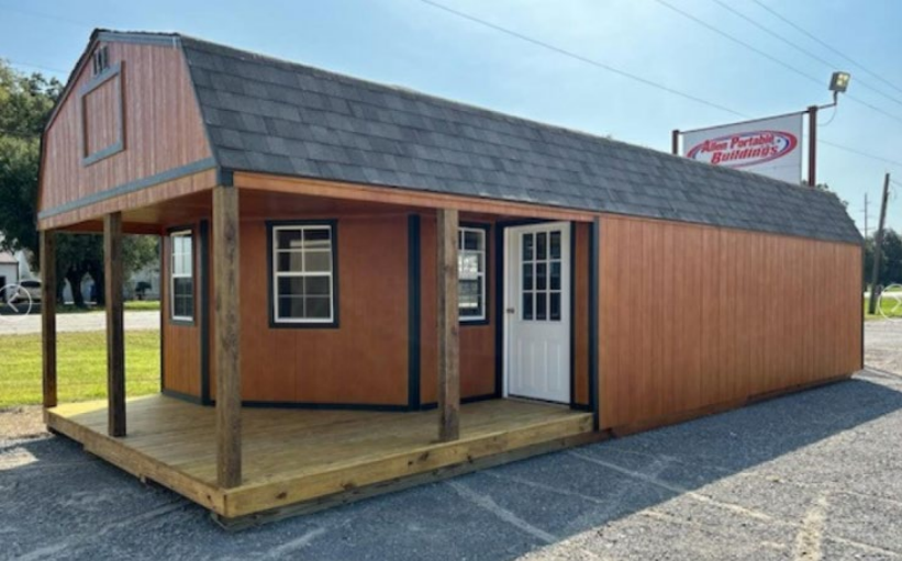 Brown shed with a porch and a dark gray roof. Outdoors on a sunny day.