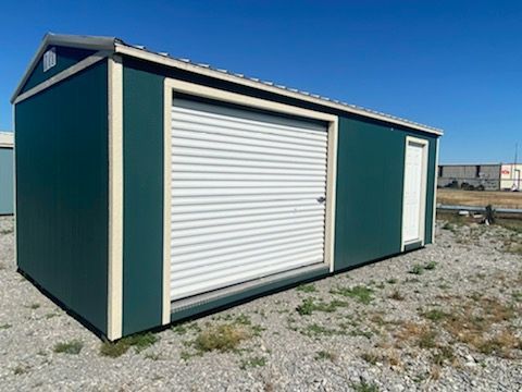 Green storage shed with a roll-up door, a white door, and cream trim against a blue sky.