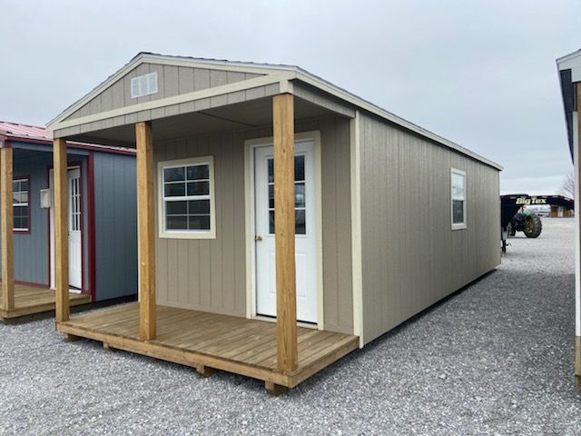 Tan shed with porch and white door and window, gravel ground.