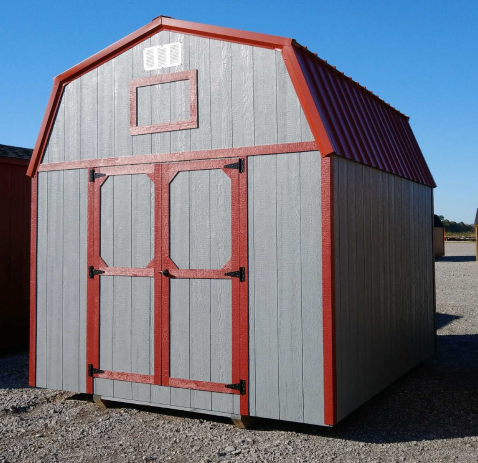Gray and red barn-style shed with double doors, red roof trim, and a small window under a blue sky.
