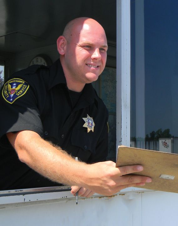 Police officer in uniform leans out of a window, holding a clipboard, smiling.