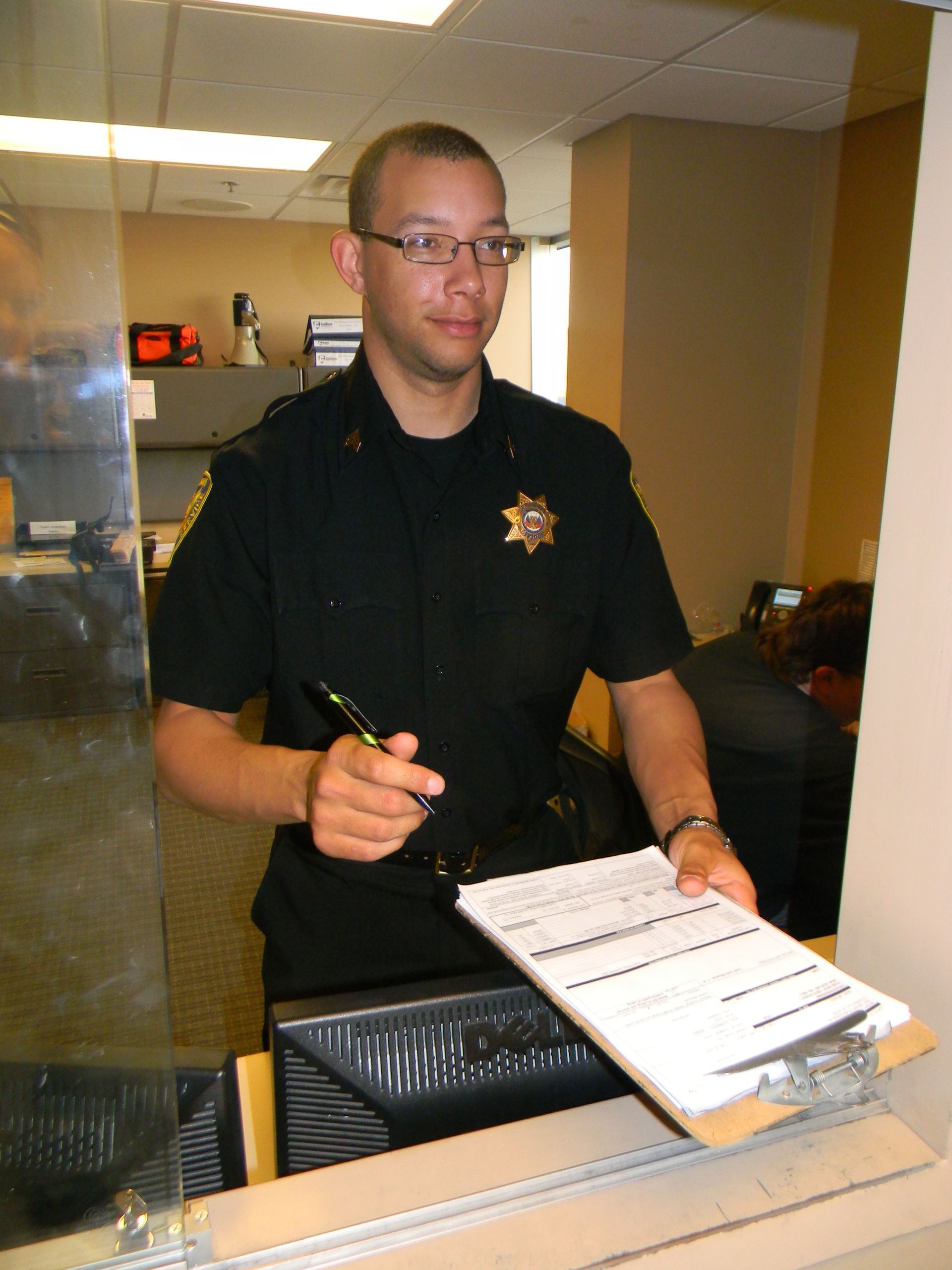 Officer in black uniform holding a clipboard and pen at a counter.