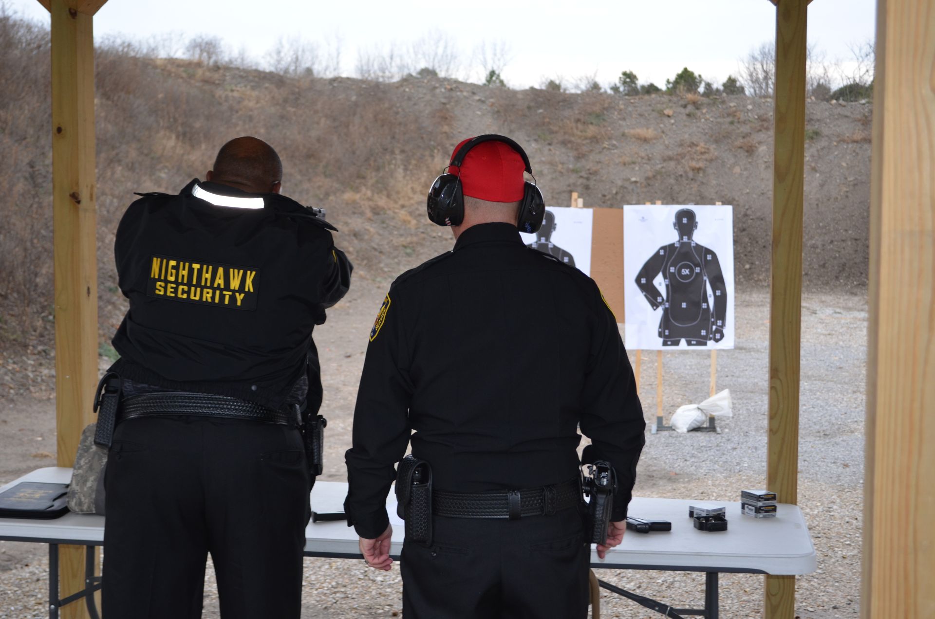 Two people wearing security uniforms practice shooting at targets on a firing range.