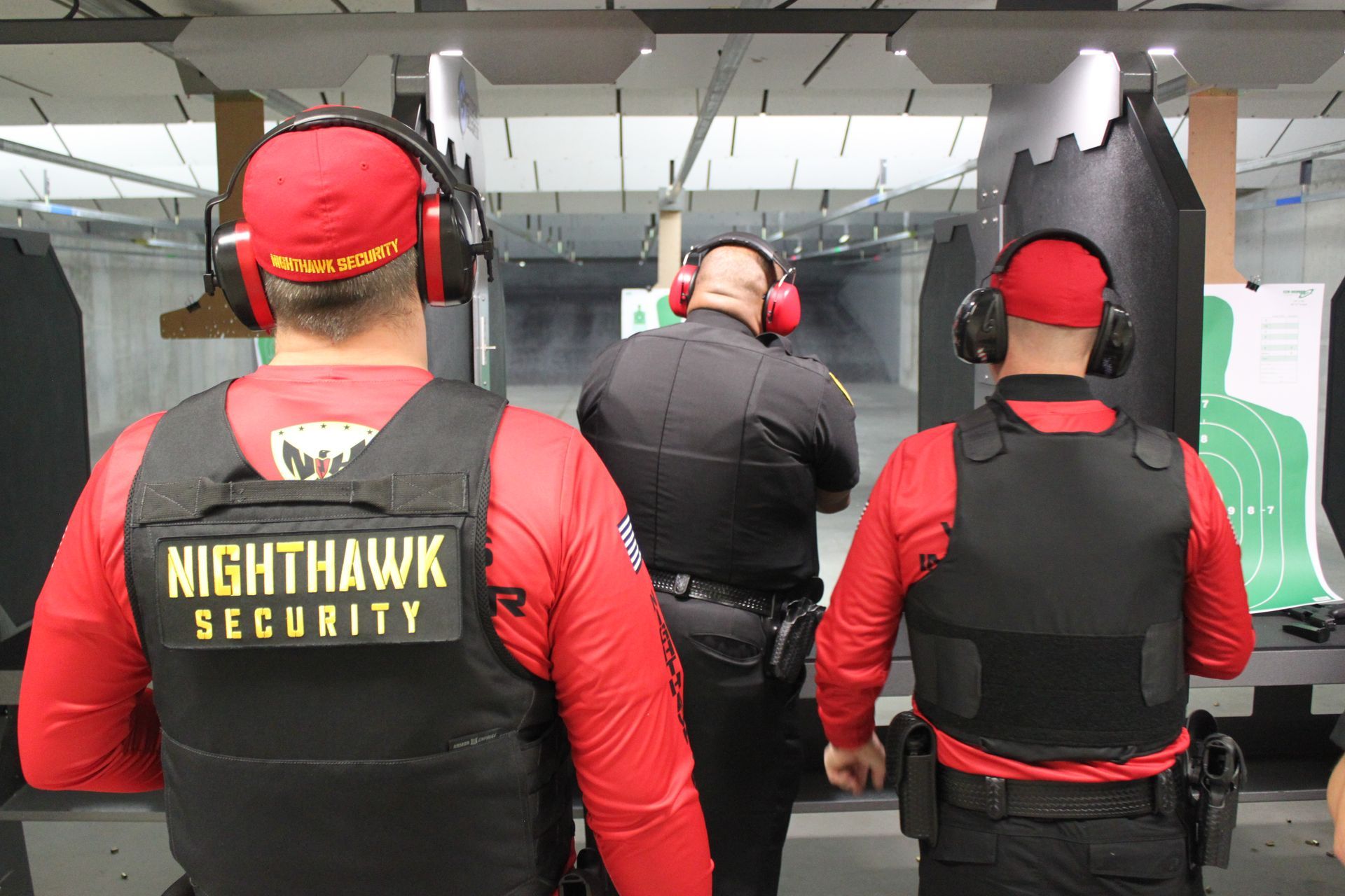 Three people at a shooting range, two in red shirts and vests labeled 