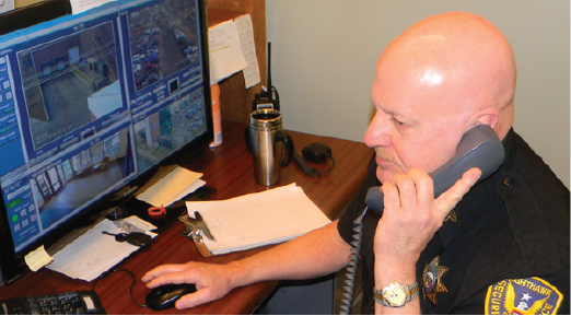 Three people at a shooting range, two in red shirts and vests labeled 