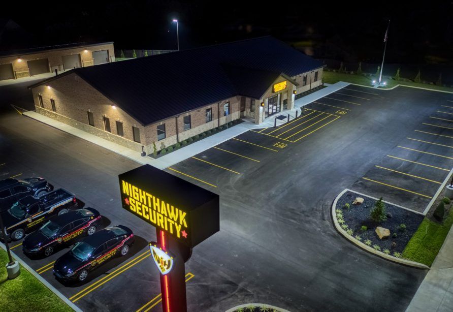 Night view of Nighthawk Security building and sign, with several black cars parked nearby.