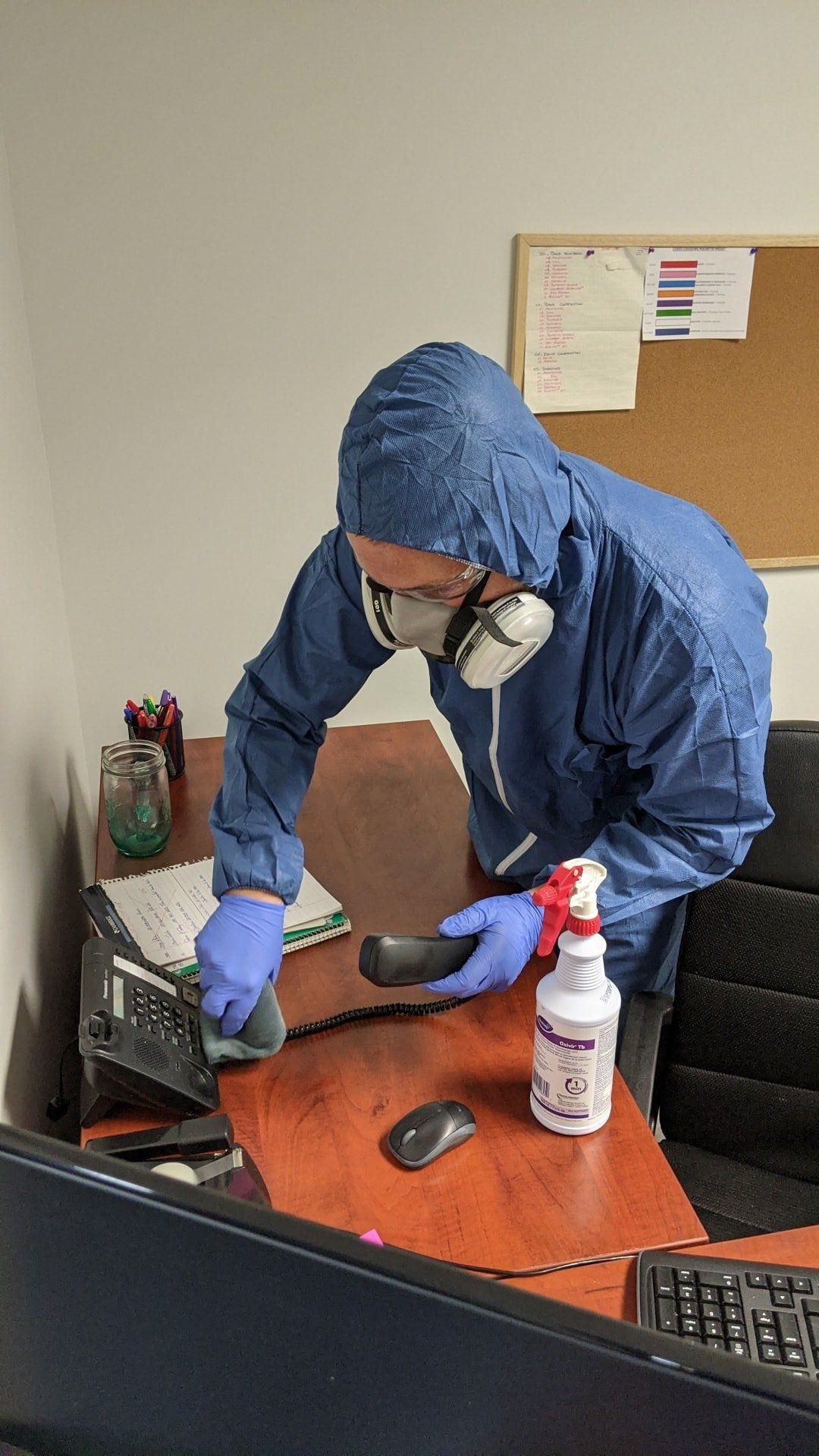 Un homme en combinaison de protection nettoie un bureau avec un vaporisateur.