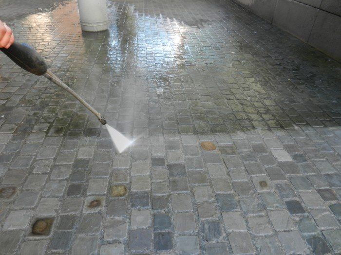 Une personne utilise un nettoyeur haute pression pour nettoyer un sol en briques.