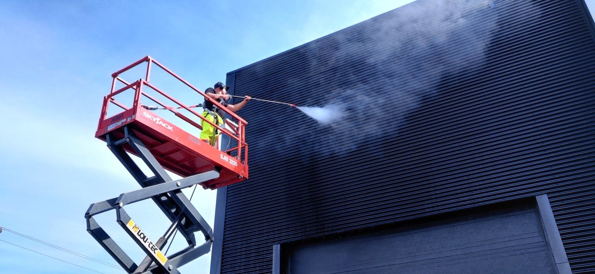 Un homme nettoie un bâtiment avec un nettoyeur haute pression.