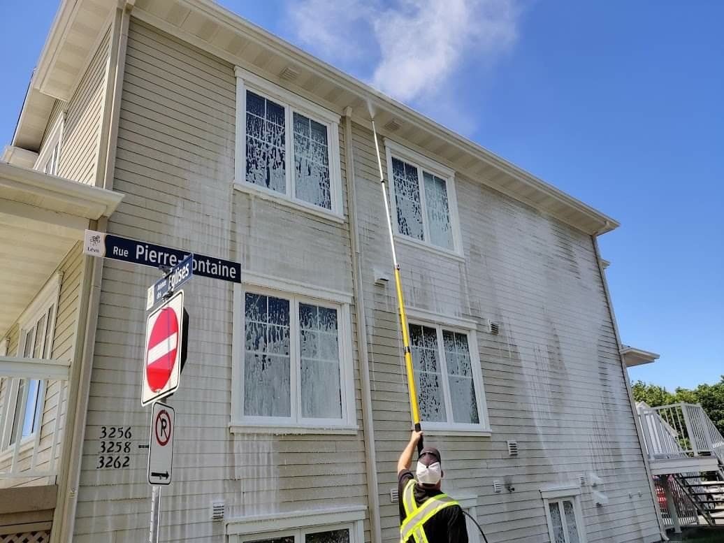 Un homme nettoie le côté d'un bâtiment avec un nettoyeur haute pression.