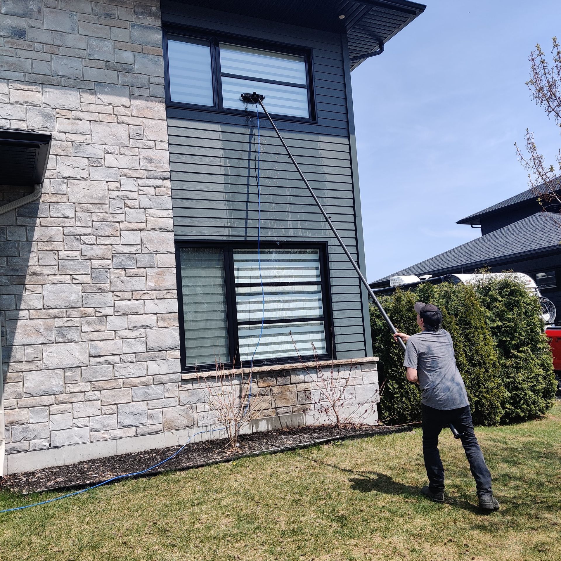 Un homme nettoie les fenêtres d'une maison avec un tuyau.