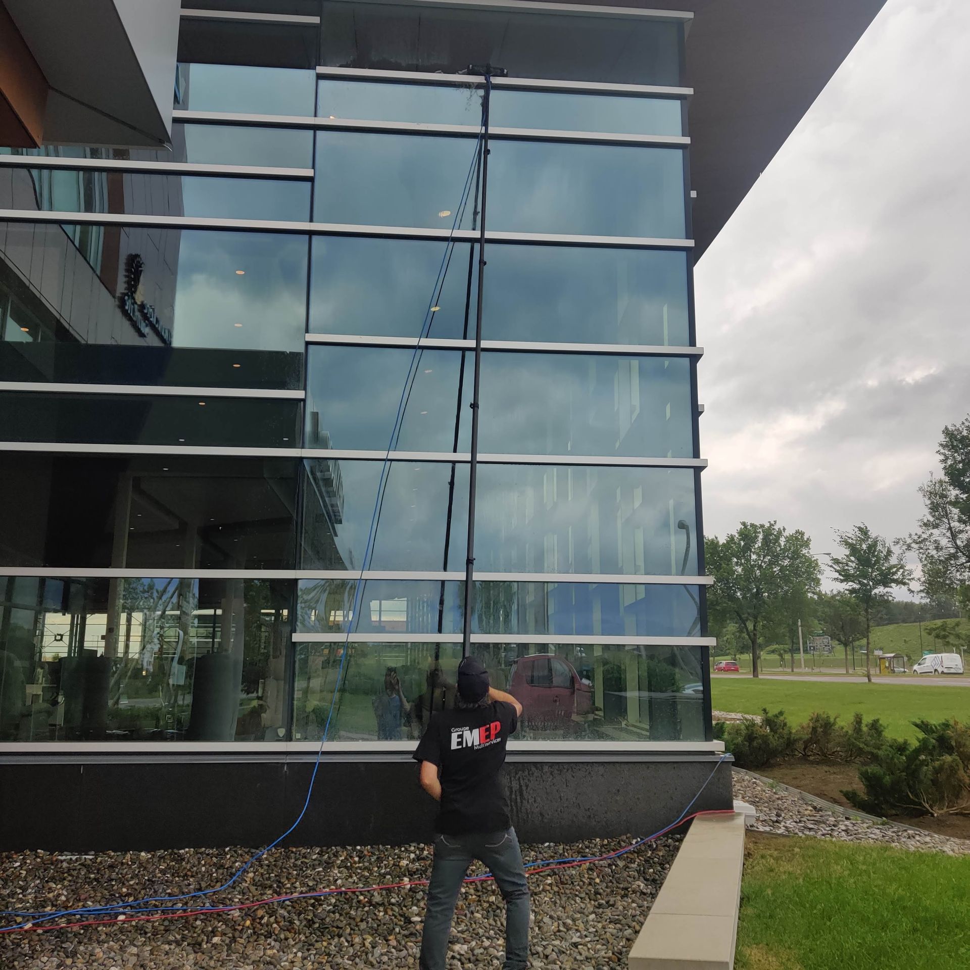Un homme nettoie les fenêtres d'un bâtiment avec un tuyau sur lequel est écrit fmc
