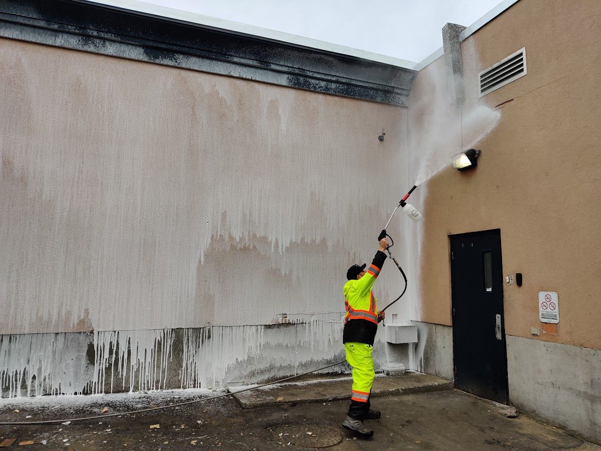 Un homme nettoie un bâtiment avec un nettoyeur haute pression.