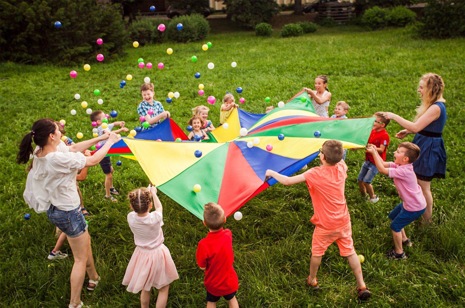 children waving  rainbow parachute full of colored balls
