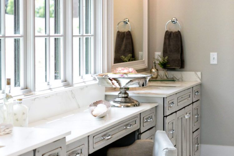 Bright bathroom vanity with large windows, gray cabinets, a marble countertop, and gold fixtures