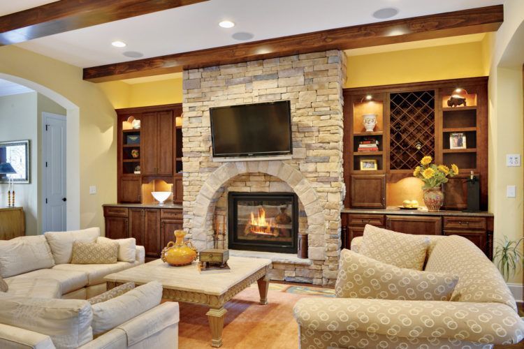Cozy living room with stone fireplace, mounted TV, built-in shelves, and beige sofas