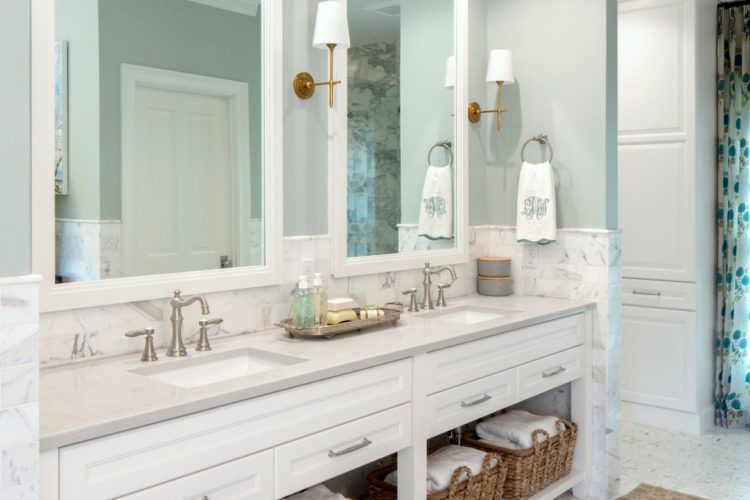 Bright white bathroom vanity with double mirrors, brass sconces, and woven baskets underneath