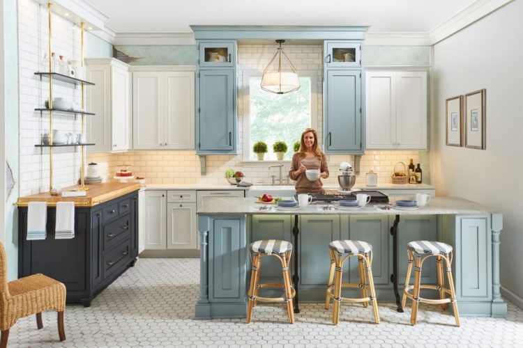 Bright kitchen with blue cabinets, white island, and a woman standing at the counter.