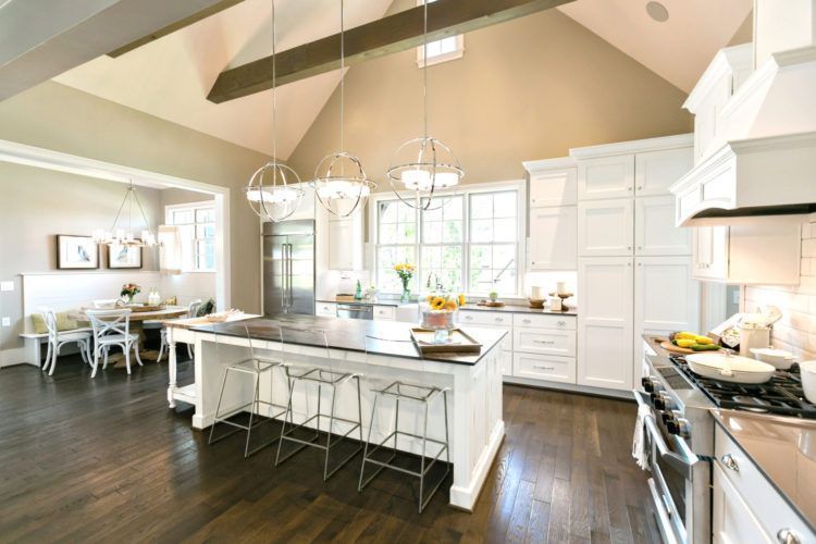 Bright white modern kitchen with island, pendant lights, dark wood floors, and dining area by windows