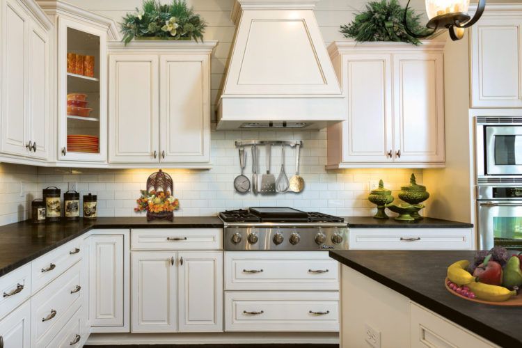 Bright white kitchen with black countertops, stainless stove, and decorative plants on top of cabinets.