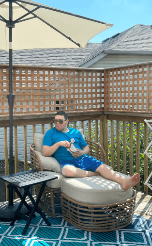 A man is sitting in a chair on a deck under an umbrella.