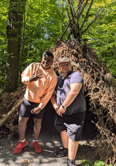 Two men are standing next to each other in the woods holding hands.