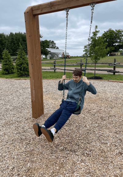 A man is sitting on a swing in a park.