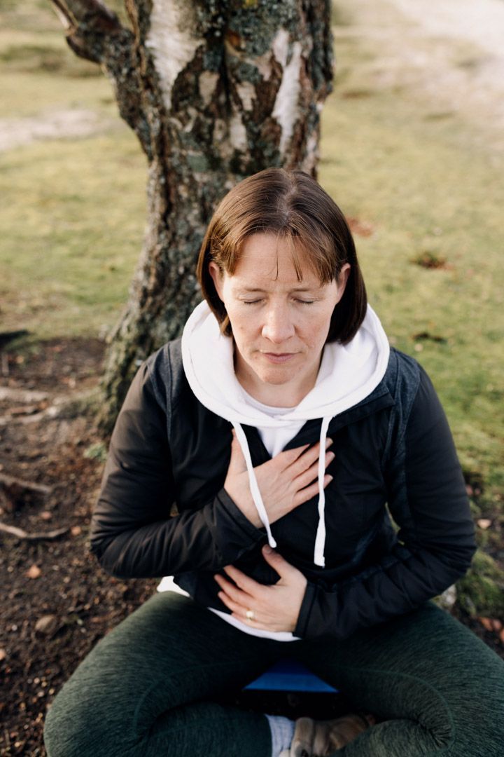 photograph of Katie sitting cross legged by a tree meditating with eyes closed