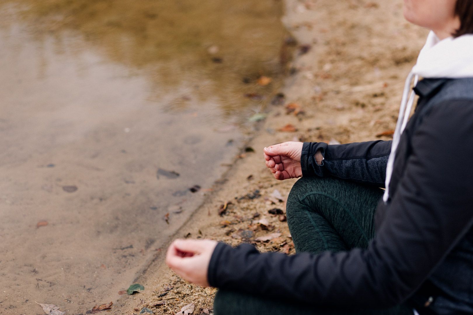 A photo of a lady resting her hands on her lap by a lake