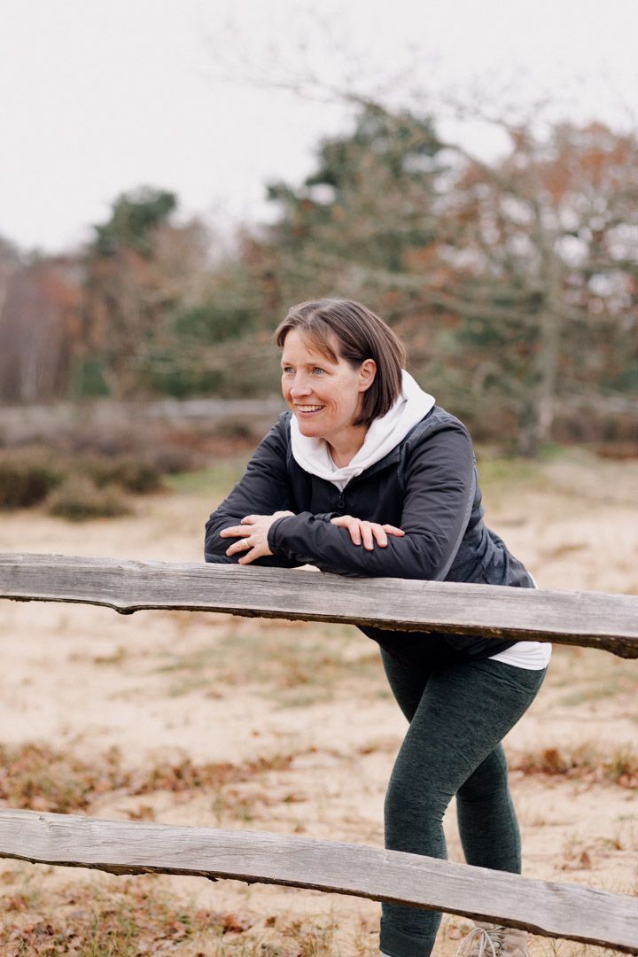 Photo of a smiling lady leaning on a fence with trees behind